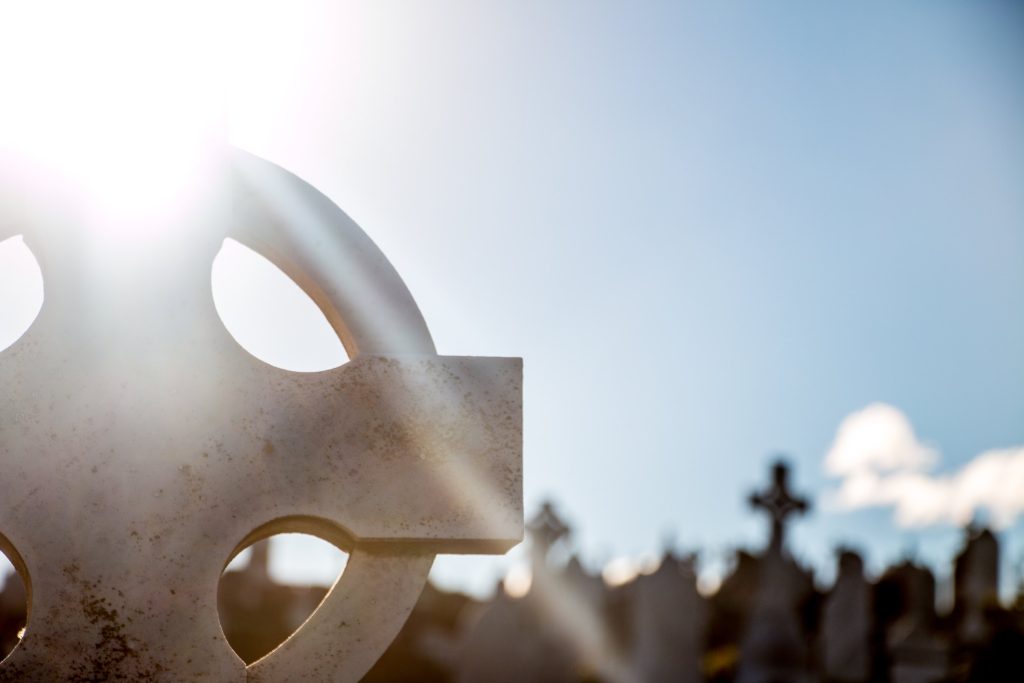 A weathered stone cross against the sky with graves behind