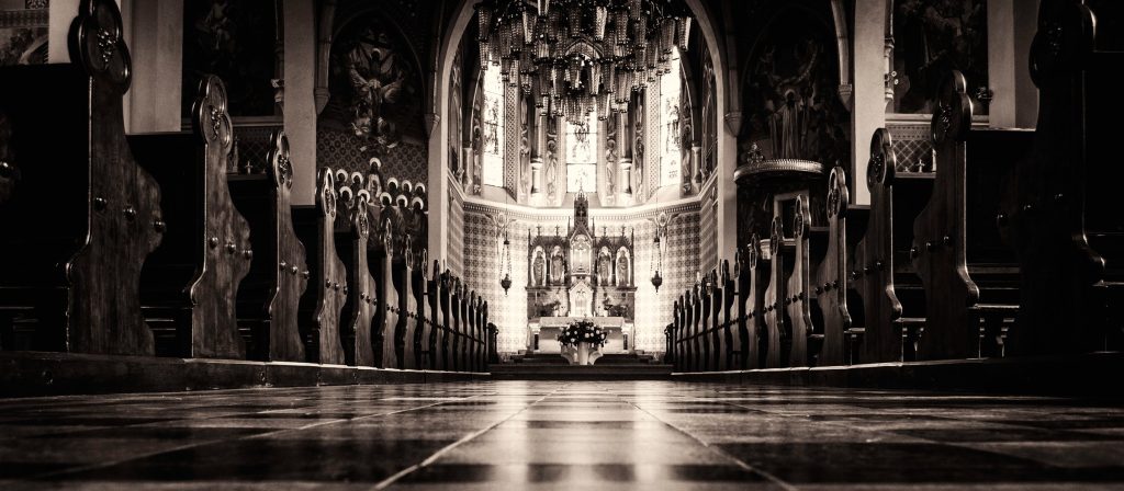 A dim church interior in monochrome, light falling down the nave